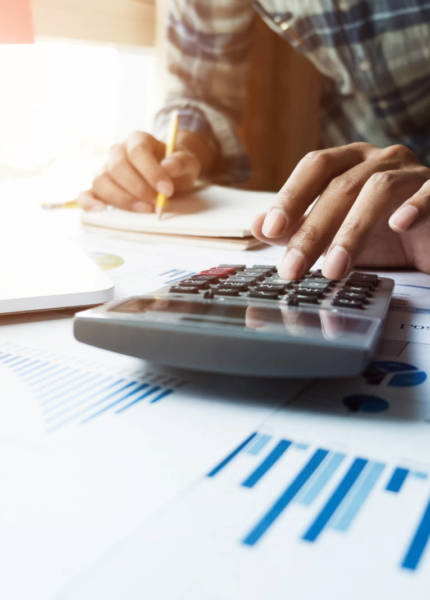 Close up of businessman or accountant hand holding pen working on calculator and laptop computer to calculate business data during make note at notepad, accountancy document at office, business financial concept